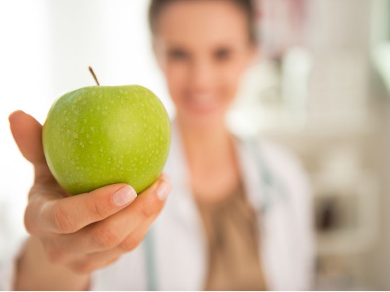 Zahnärztin hält grünen mit Apfel in Richtung Kamera