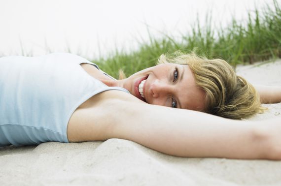 Frau mittleren Altes liegt ausgestreckt im Sand vor einer Düne