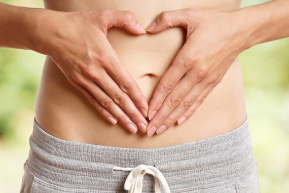 Frau bildet mit ihren auf dem Bauch liegenden Händen ein Herz