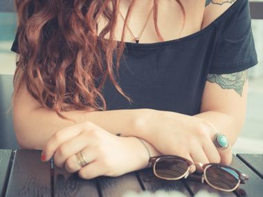 Sitzende junge Frau mit ihrer Sonnenbrille vor ihr auf dem Tisch