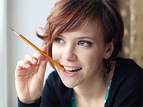Junge Frau, die nachdenkend auf einem Bleistift kaut.