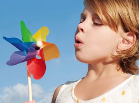 Mädchen pustet kräftig gegen ein Windrädchen.