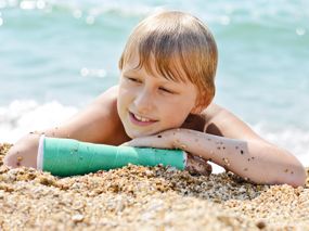 Eine Junge mit eingegipstem Unterarm liegt am Strand und macht einen glücklichen Eindruck.