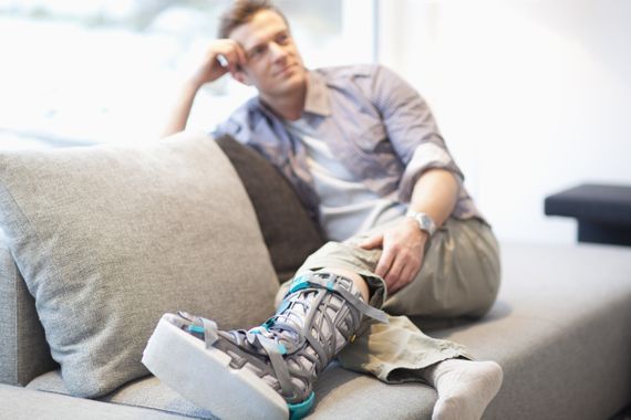 Mann mit gebrochenem Bein liegt auf der Couch.