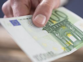 Eine Hand reicht einen Hunderteuroschein in Richtung Kamera