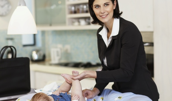 Frau in Businesskleidung wickelt ihr Kind