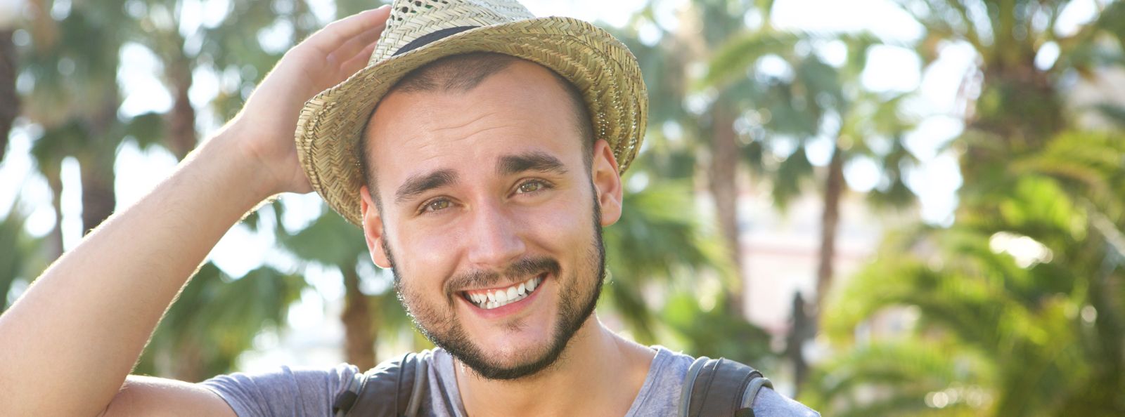 Junger Mann mit Strohhut guckt verschmitzt in die Kamera