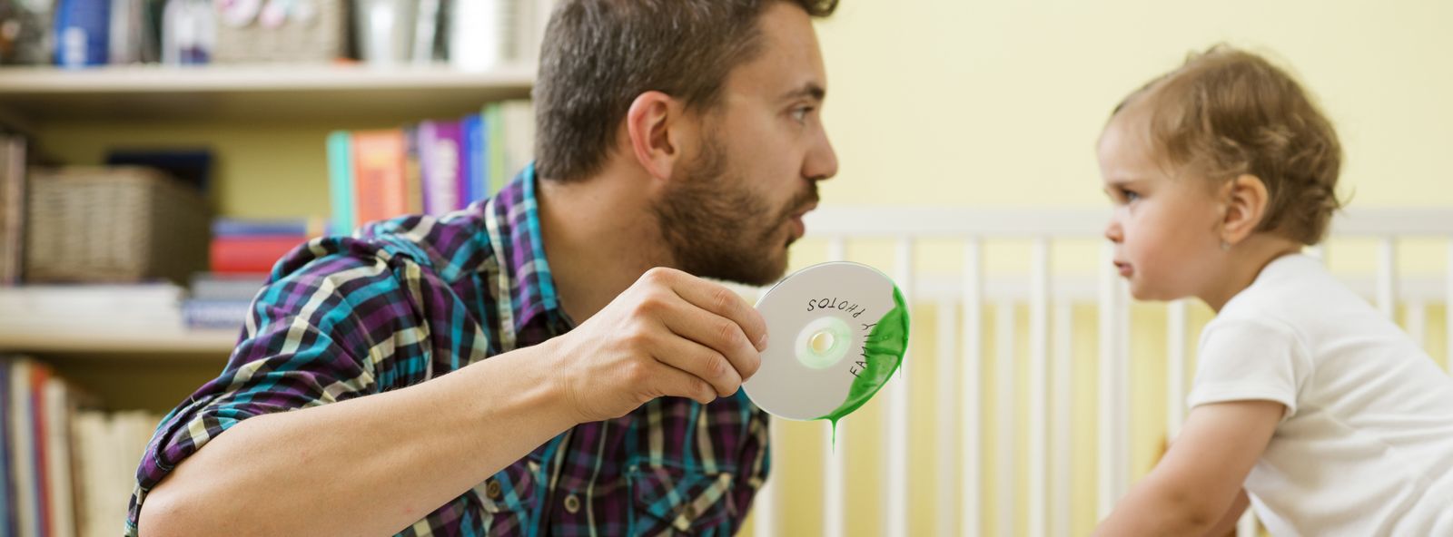 Vater redet streng mit seiner Tochter und hält eine CD die in grüne Farbe getaucht wurde in der Hand