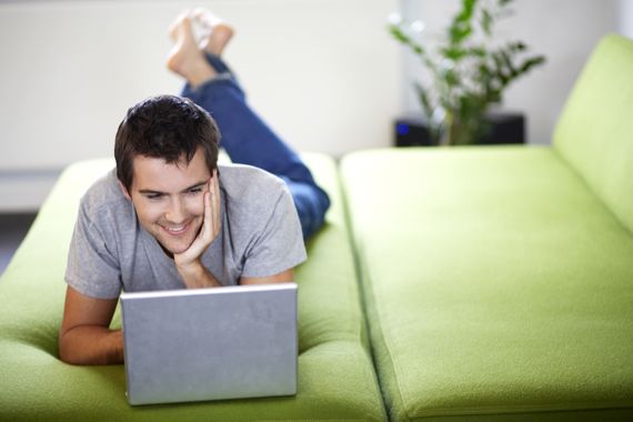 Mann liegt mit Laptop auf grünem Sofa