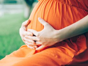 Schwangere im orangenen Kleid sitzt enstpannt im Freien