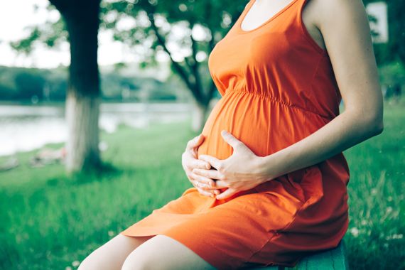 Schwangere im orangenen Kleid sitzt entspannt im Freien