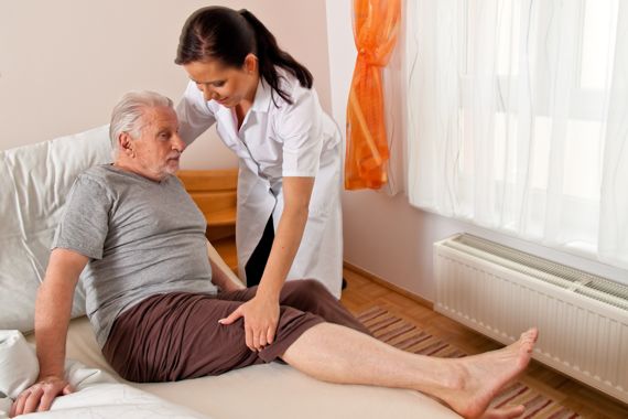 Pflegerin hilft altem Mann ins Bett