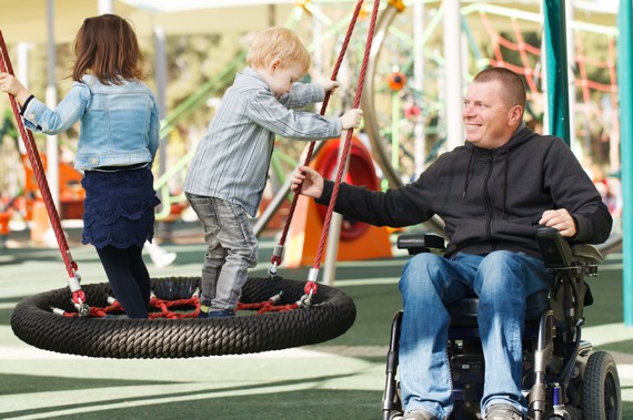 Mann im Rollstuhl mit Kindern auf Spielplatz