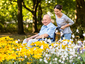 Frau schiebt Senior im Rollstuhl durch Park